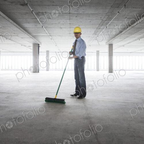 Asian businessman cleaning up with a broom in a large empty raw office space. Asian businessman cleaning up with a broom in a large empty raw office space.
