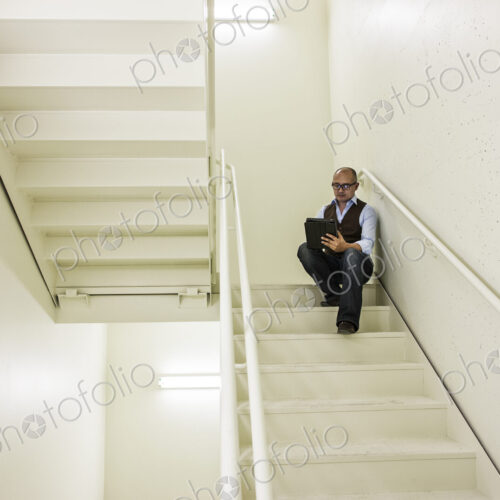 Asian businessman sitting in a stairwell working on a notebook computer.