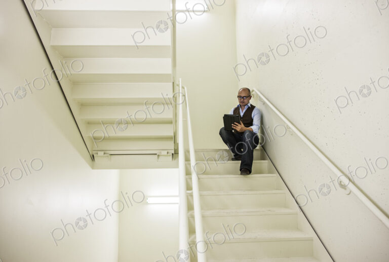Asian businessman sitting in a stairwell working on a notebook computer.