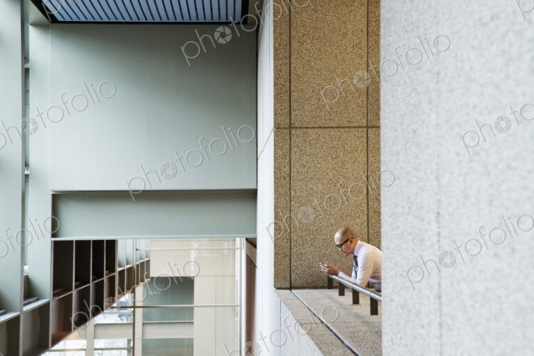 Asian businessman standing in a convention center hallway working on a notebook computer.