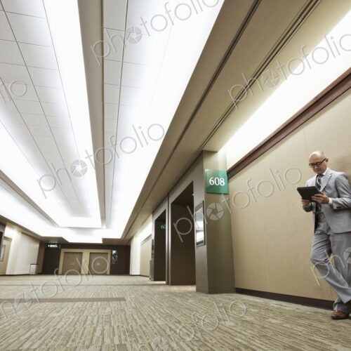 Asian businessman standing in a convention center hallway working on a notebook computer. Asian businessman standing in a convention center hallway working on a notebook computer.