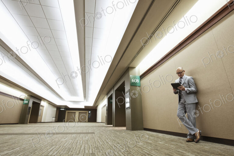 Asian businessman standing in a convention center hallway working on a notebook computer.