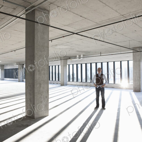Asian businessman standing in a large empty raw office space. Asian businessman standing in a large empty raw office space.