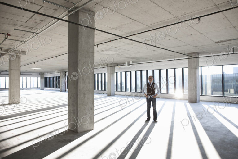 Asian businessman standing in a large empty raw office space.