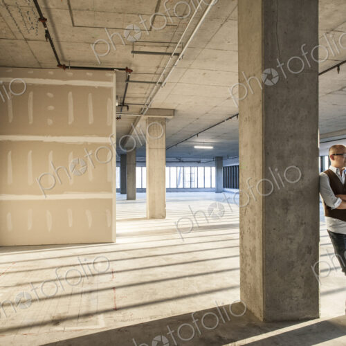 Asian businessman standing in a large empty raw office space.