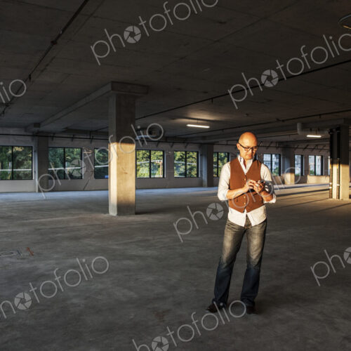 Asian businessman standing in the middle of a large empty raw office space and lit by…