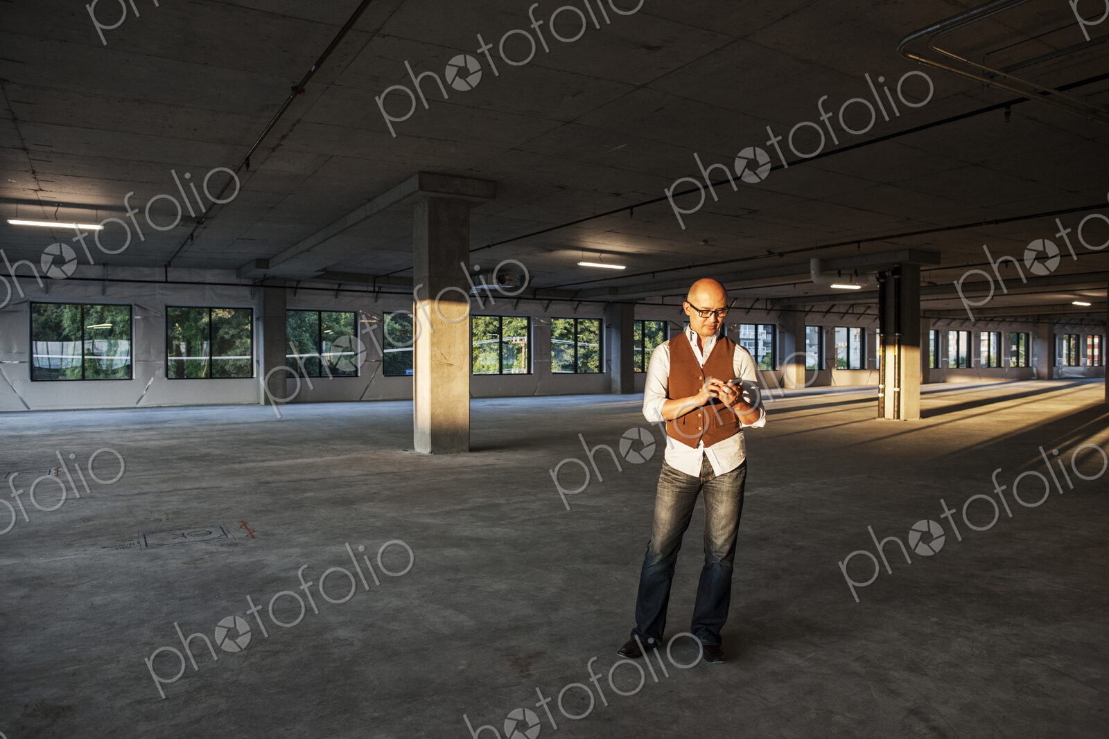 Asian businessman standing in the middle of a large empty raw office space and lit by…