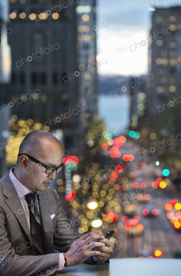 Asian businessman working on his phone by a window with city view