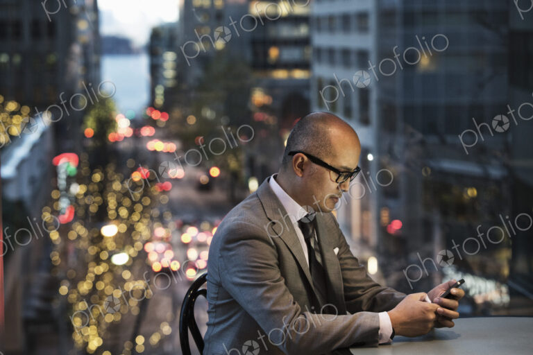 Asian businessman working on his phone by a window with city view