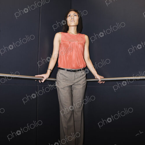 Asian businesswoman standing in the corner of an elevator in a large office building.