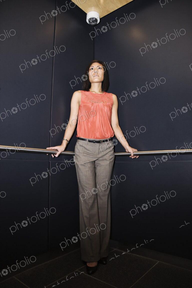 Asian businesswoman standing in the corner of an elevator in a large office building.