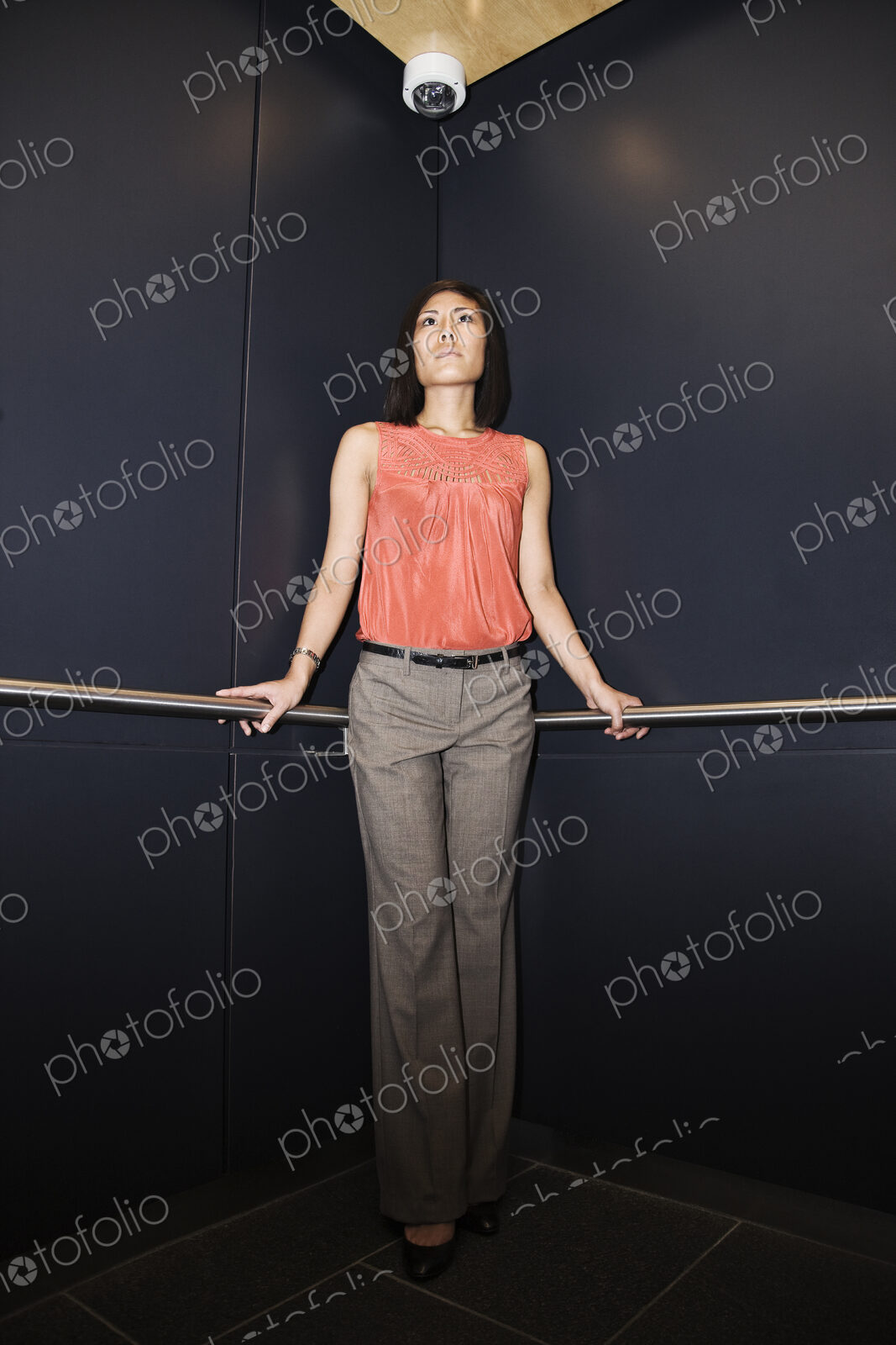 Asian businesswoman standing in the corner of an elevator in a large office building.
