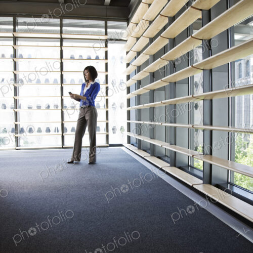 Asian businesswoman texting from the lobby of a large office building.