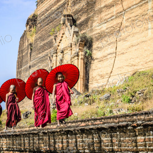 Asian children with parasols balancing on stone wall Asian children with parasols balancing on stone wall