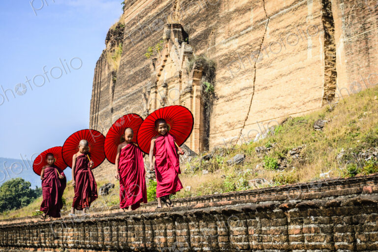 Asian children with parasols balancing on stone wall