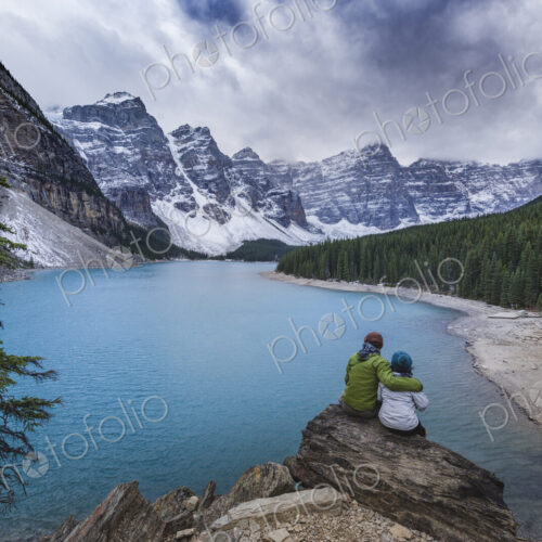 Asian couple sitting on rock admiring scenic view of mountain lake Asian couple sitting on rock admiring scenic view of mountain lake