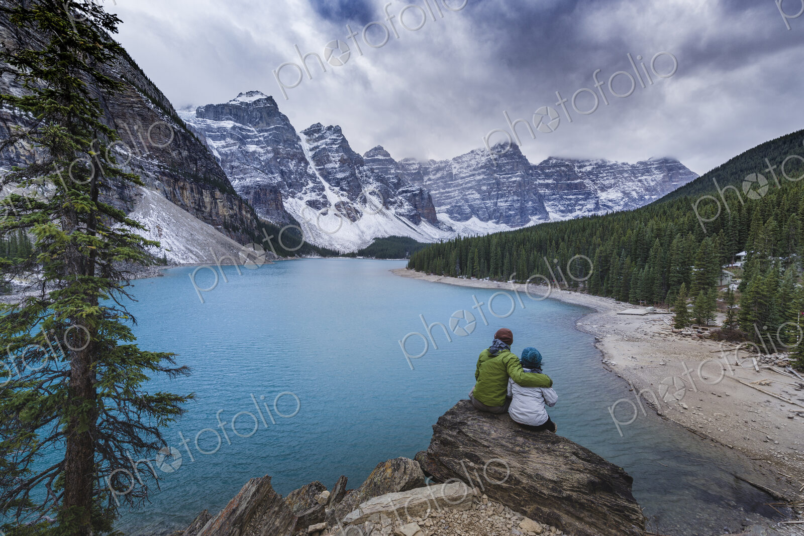 Asian couple sitting on rock admiring scenic view of mountain lake