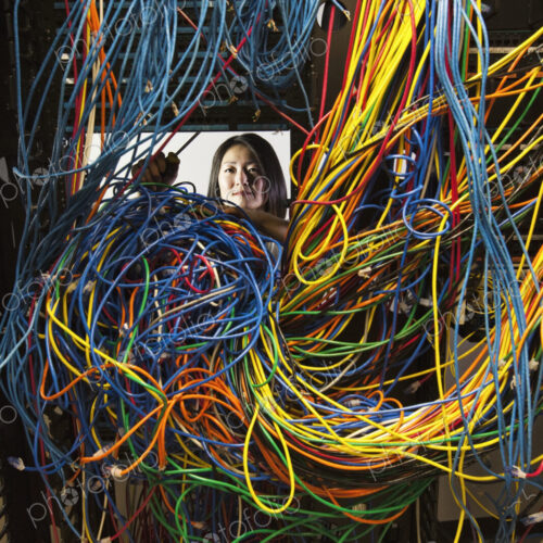 Asian female technician woking on a tangled mess of CAT 5 cables in a server room.