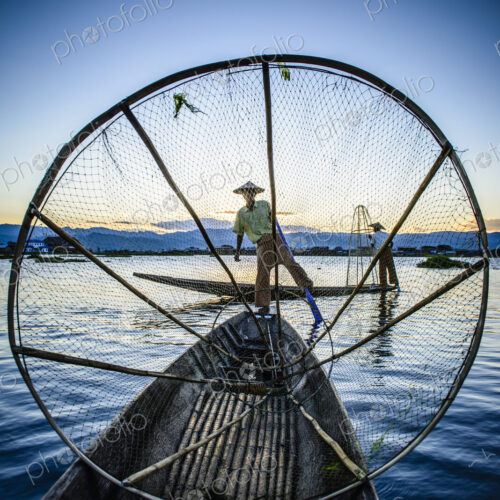 Asian fisherman using fishing net in canoe on river Asian fisherman using fishing net in canoe on river