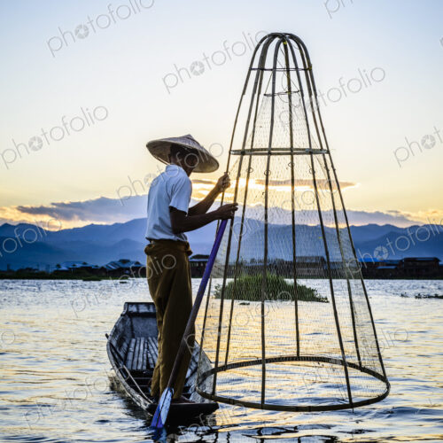 Asian fisherman using fishing net in canoe on river Asian fisherman using fishing net in canoe on river