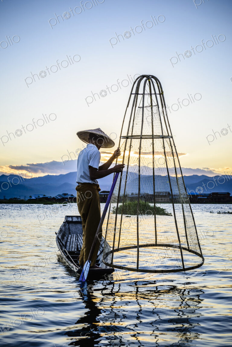 Asian fisherman using fishing net in canoe on river