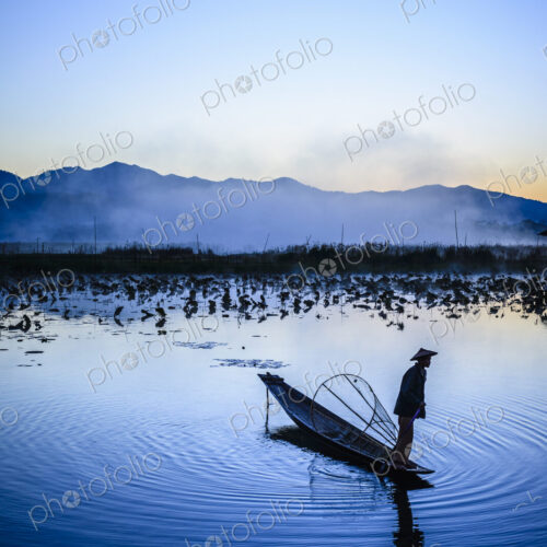 Asian fisherman using fishing net in canoe on river Asian fisherman using fishing net in canoe on river