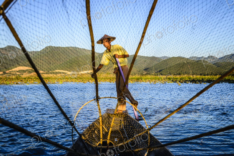 Asian fisherman using fishing net in canoes on river