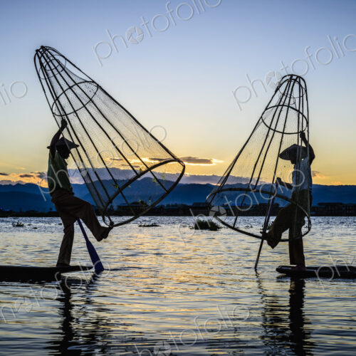 Asian fishermen using fishing nets in canoe on river Asian fishermen using fishing nets in canoe on river