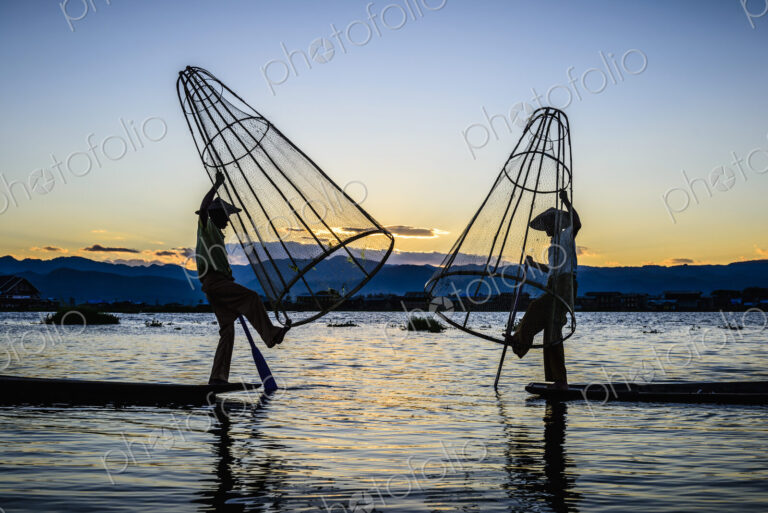 Asian fishermen using fishing nets in canoe on river
