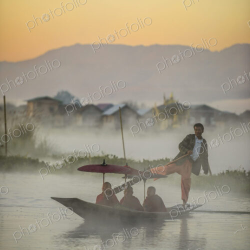 Asian gondolier rowing monks in canoe on river Asian gondolier rowing monks in canoe on river