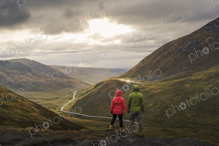 Asian hikers holding hands admiring scenic view of valley