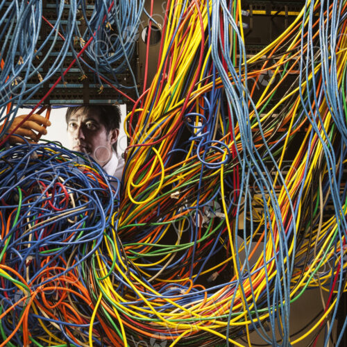 Asian male technician working on a tangled mess of CAT 5 cables in a server room.