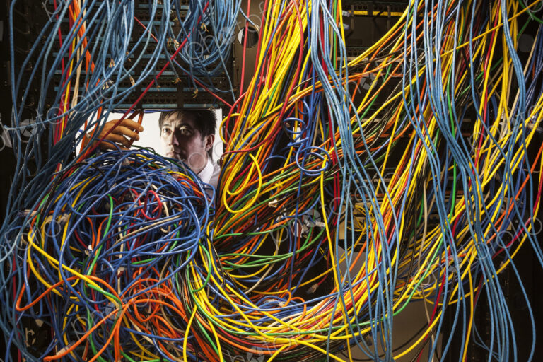 Asian male technician working on a tangled mess of CAT 5 cables in a server room.