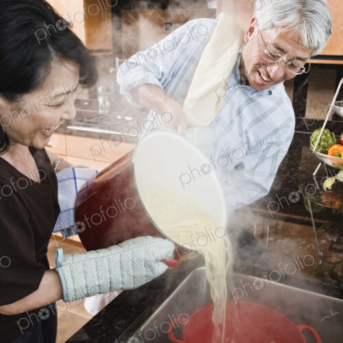 Asian man and woman pareparing a healthy pasta meal in their kitchen. Asian man and woman pareparing a healthy pasta meal in their kitchen.