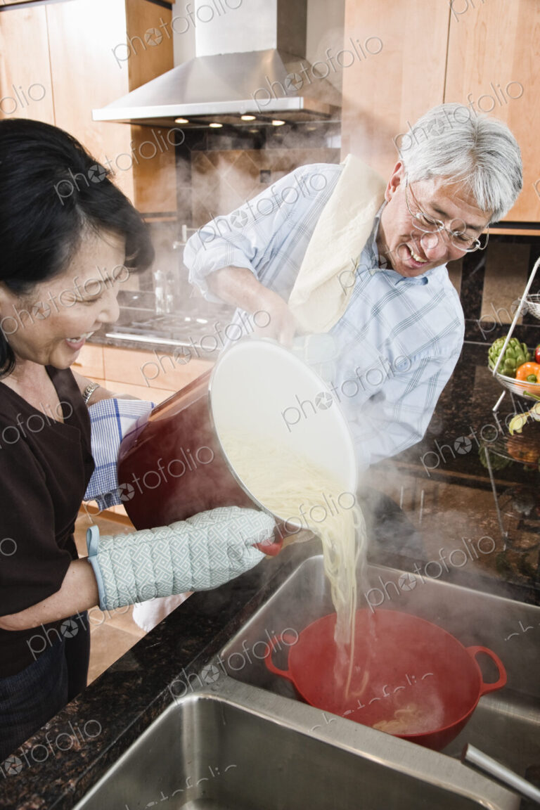 Asian man and woman pareparing a healthy pasta meal in their kitchen.