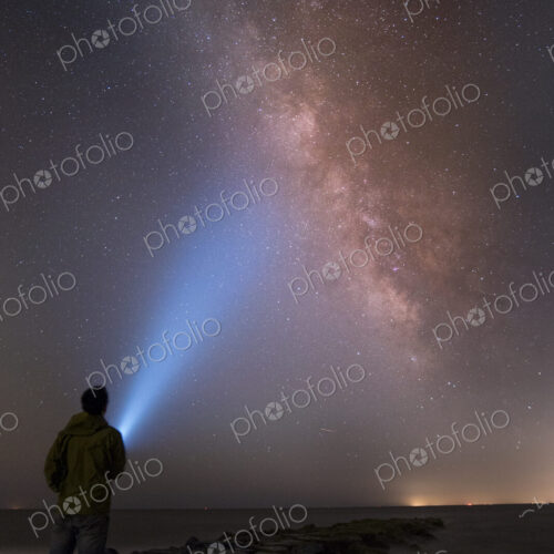 Asian man shining flashlight on starry sky