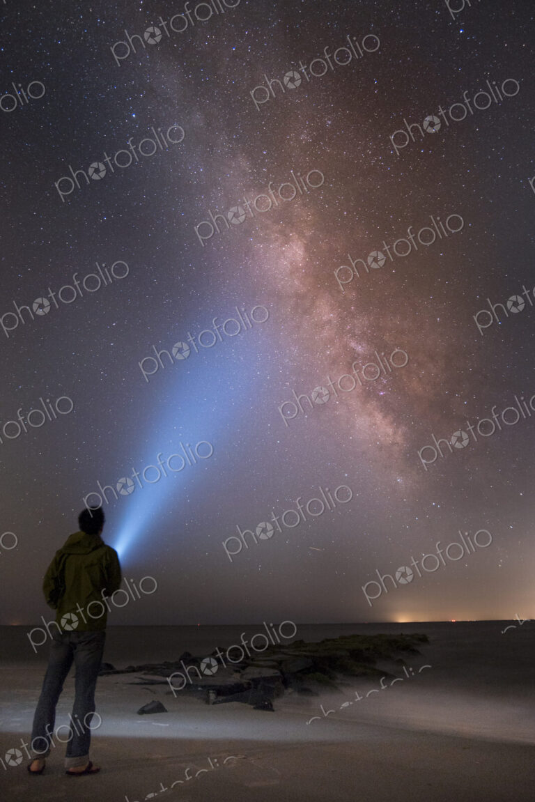 Asian man shining flashlight on starry sky