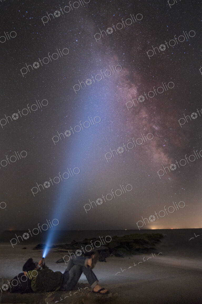 Asian man shining flashlight on starry sky