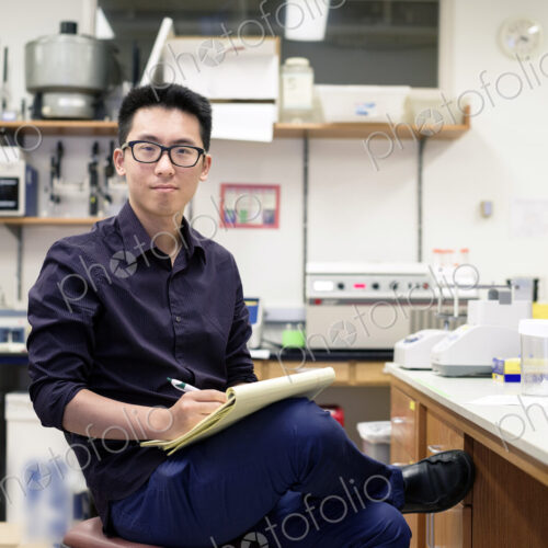 Asian man writing on notepad in electronics workshop