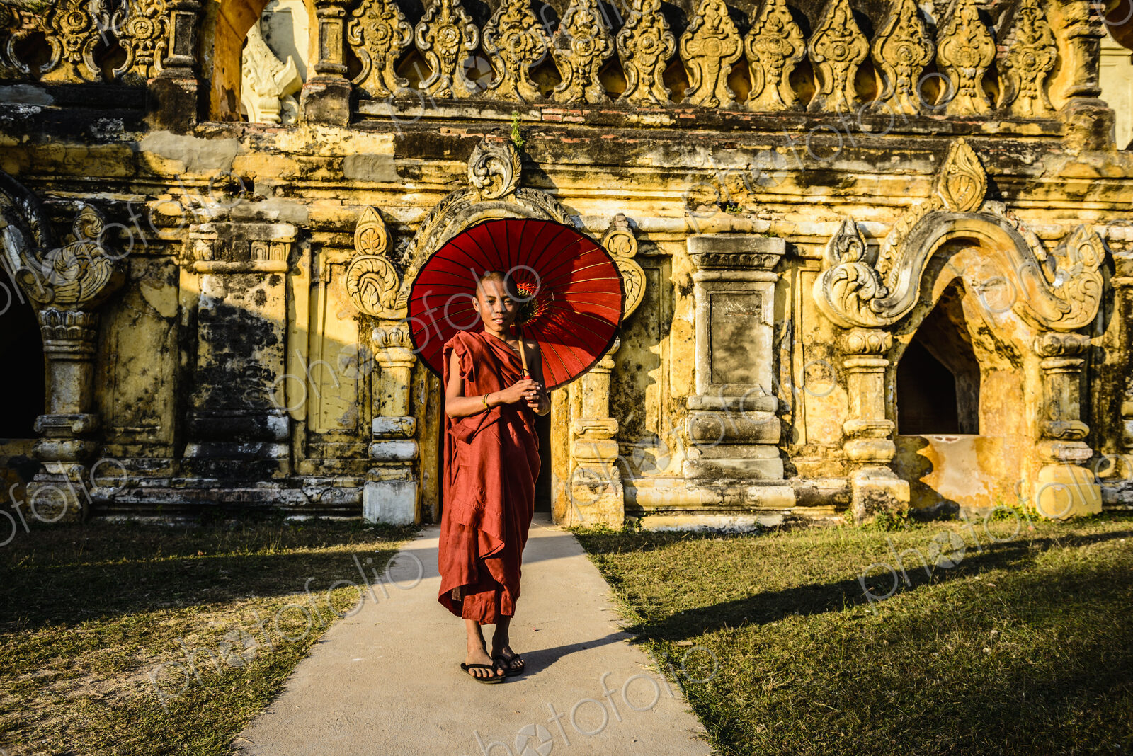 Asian monk-in-training holding parasol outside ornate temple