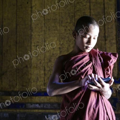 Asian monk-in-training using cell phone in temple Asian monk-in-training using cell phone in temple