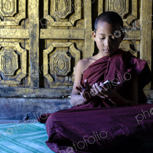Asian monk-in-training using cell phone in temple Asian monk-in-training using cell phone in temple