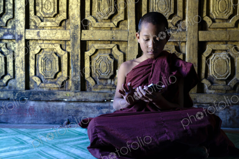 Asian monk-in-training using cell phone in temple