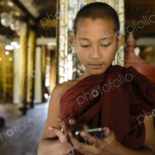 Asian monk-in-training using cell phone indoors Asian monk-in-training using cell phone indoors