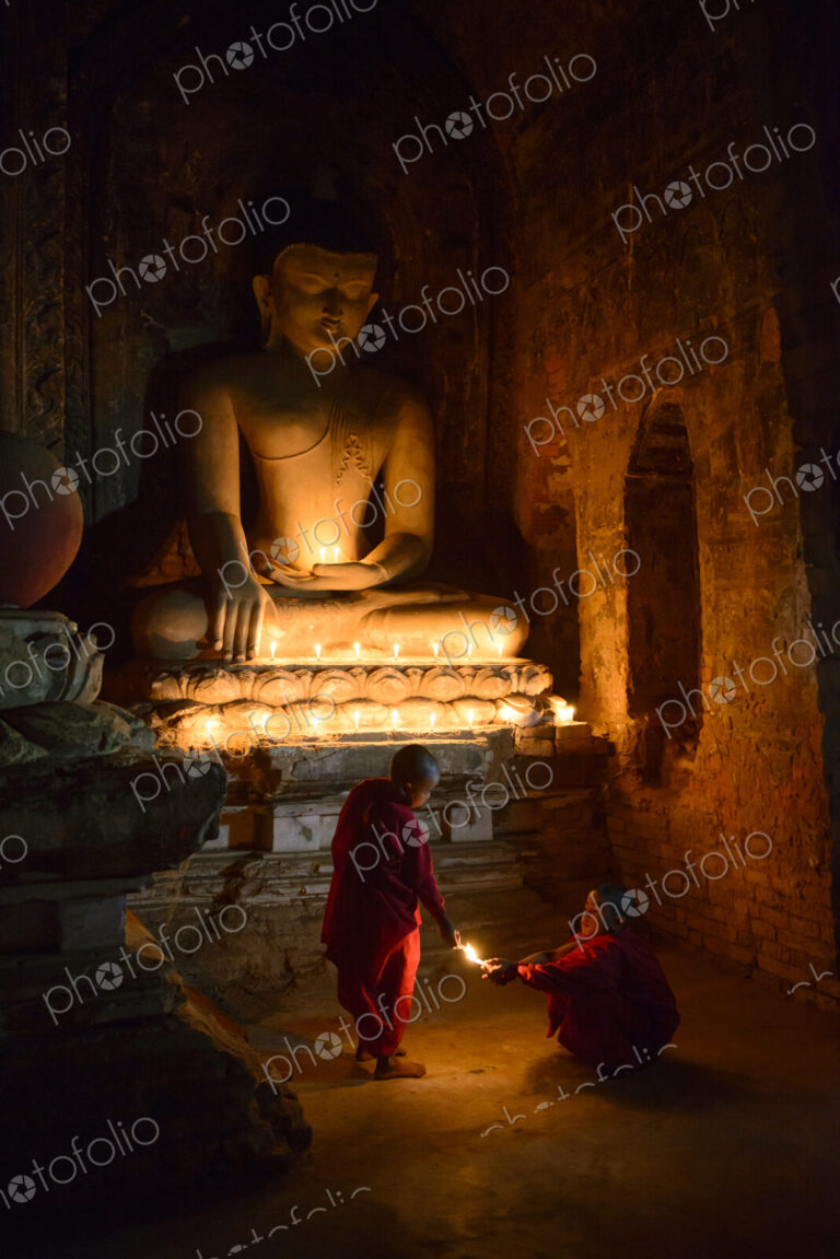 Asian monks-in-training lighting candles at Buddha shrine