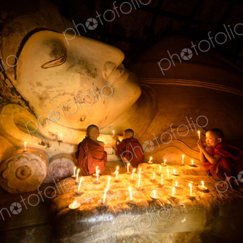 Asian monks-in-training lighting candles at Buddha statue Asian monks-in-training lighting candles at Buddha statue