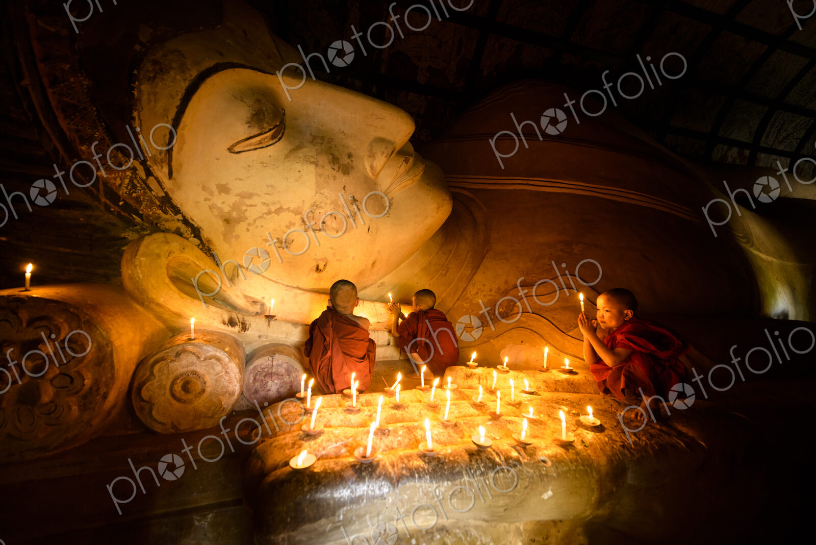 Asian monks-in-training lighting candles at Buddha statue