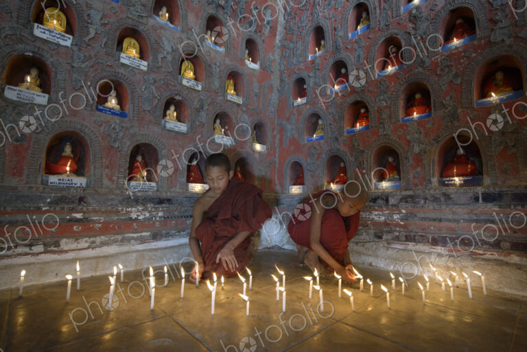 Asian monks-in-training lighting candles in ancient temple