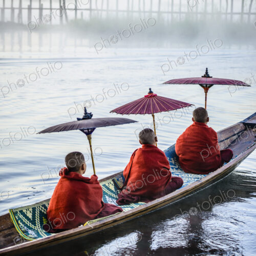 Asian monks under parasols in canoe on river Asian monks under parasols in canoe on river