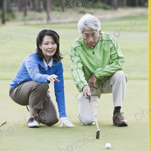 Asian senior couple taking a look at the direction of the next putt on the green.